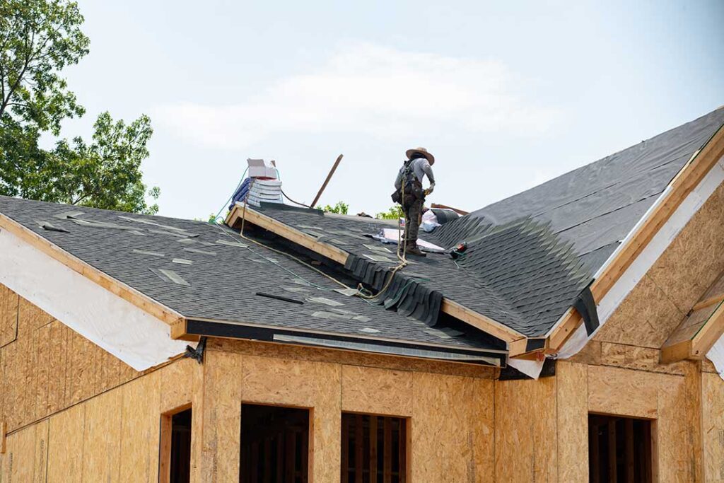 Homeowner reviews an insurance policy beside roof damage photos and a folder of maintenance records.
